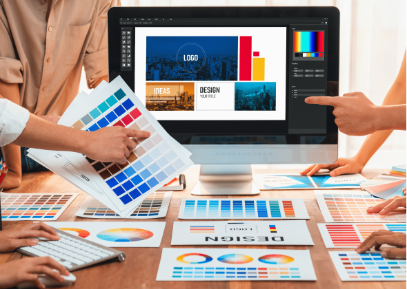 A team of 4 people choose a color palette on a desktop moniter. Text on the monitor reads logo, design, ideas